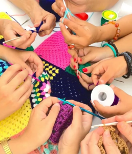 photograph of a number of hands holding yarn and crochet hooks